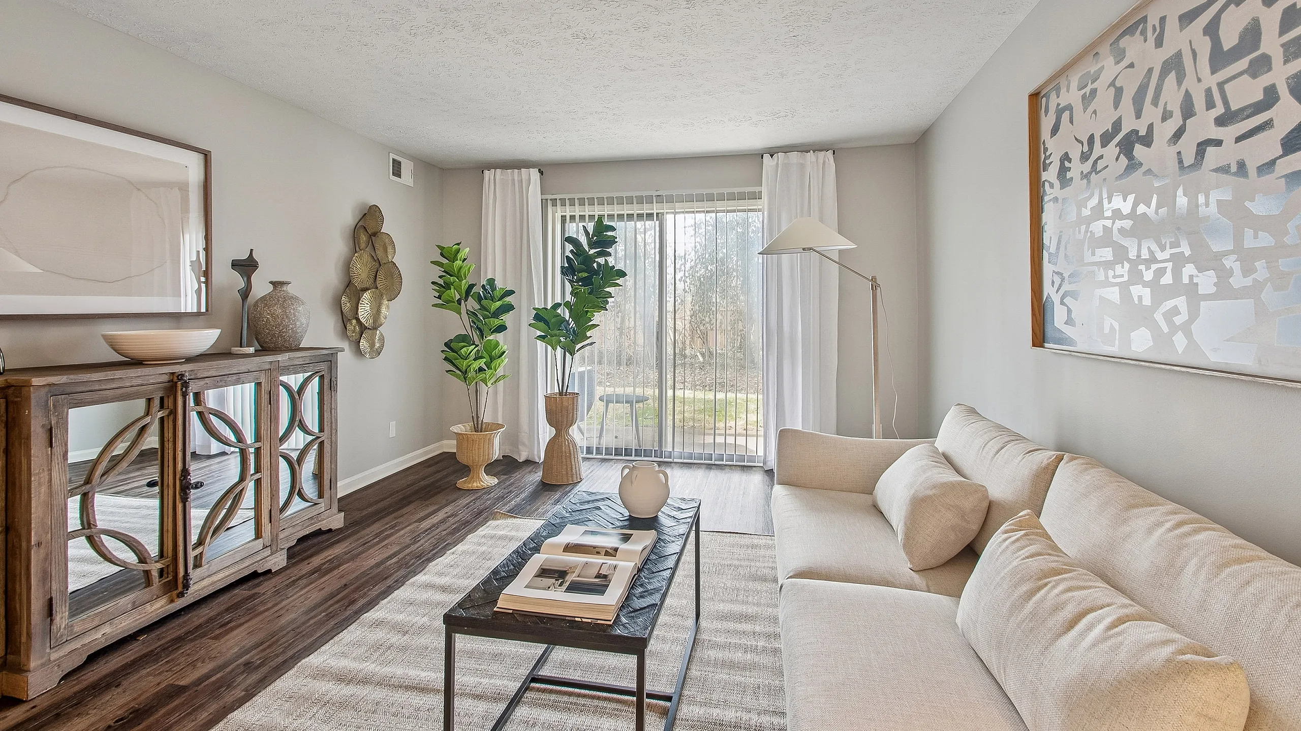 Bright and elegant living room with modern decor, featuring a cozy beige sofa and large windows allowing natural light, perfect for relaxation.