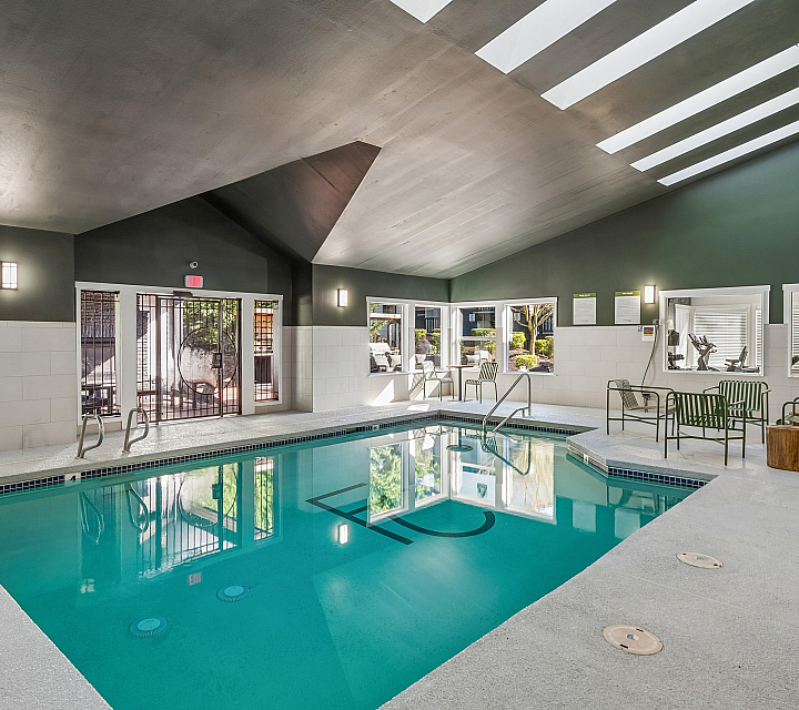 Inviting indoor swimming pool area featuring modern seating, skylights, and adjacent gym facilities.