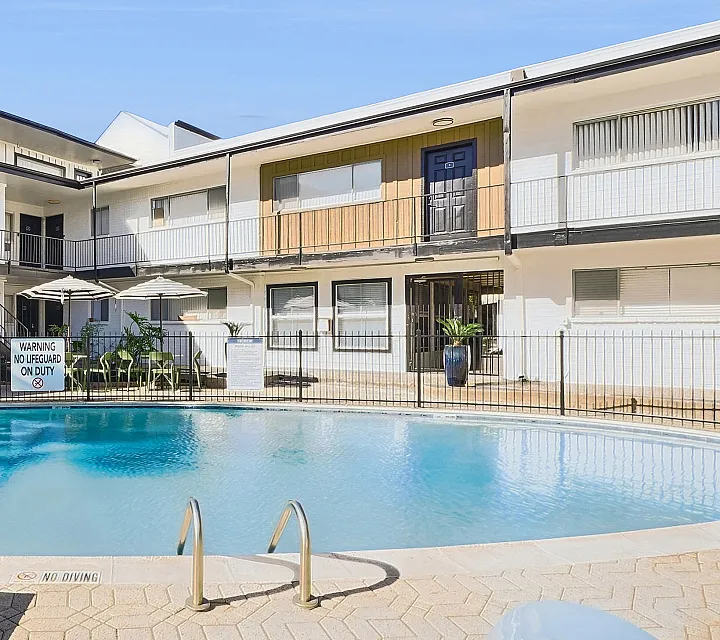 Inviting courtyard pool surrounded by modern apartments, featuring relaxing lounge chairs and vibrant greenery.