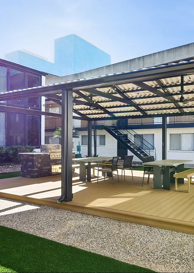Modern outdoor communal area featuring a covered barbecue setup with stylish seating, surrounded by well-maintained greenery and contemporary architecture.