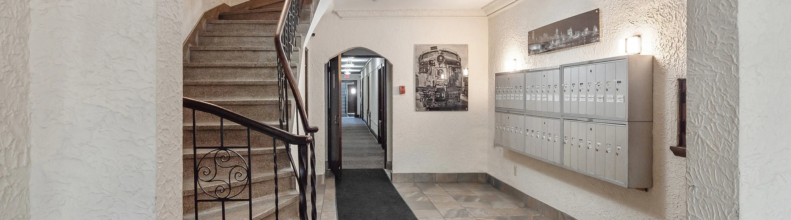 Charming apartment lobby with rustic staircase and elegant lighting, featuring stylish tile flooring and a row of neatly arranged mailboxes.