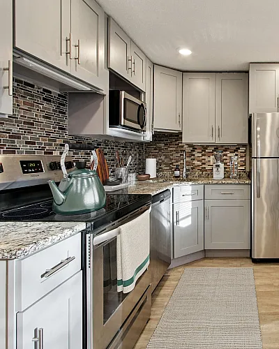 Modern kitchen with stylish gray cabinetry, sleek stainless steel appliances, and a decorative tile backsplash. Bright and spacious with natural light streaming through large windows. Perfect for culinary enthusiasts and entertaining.