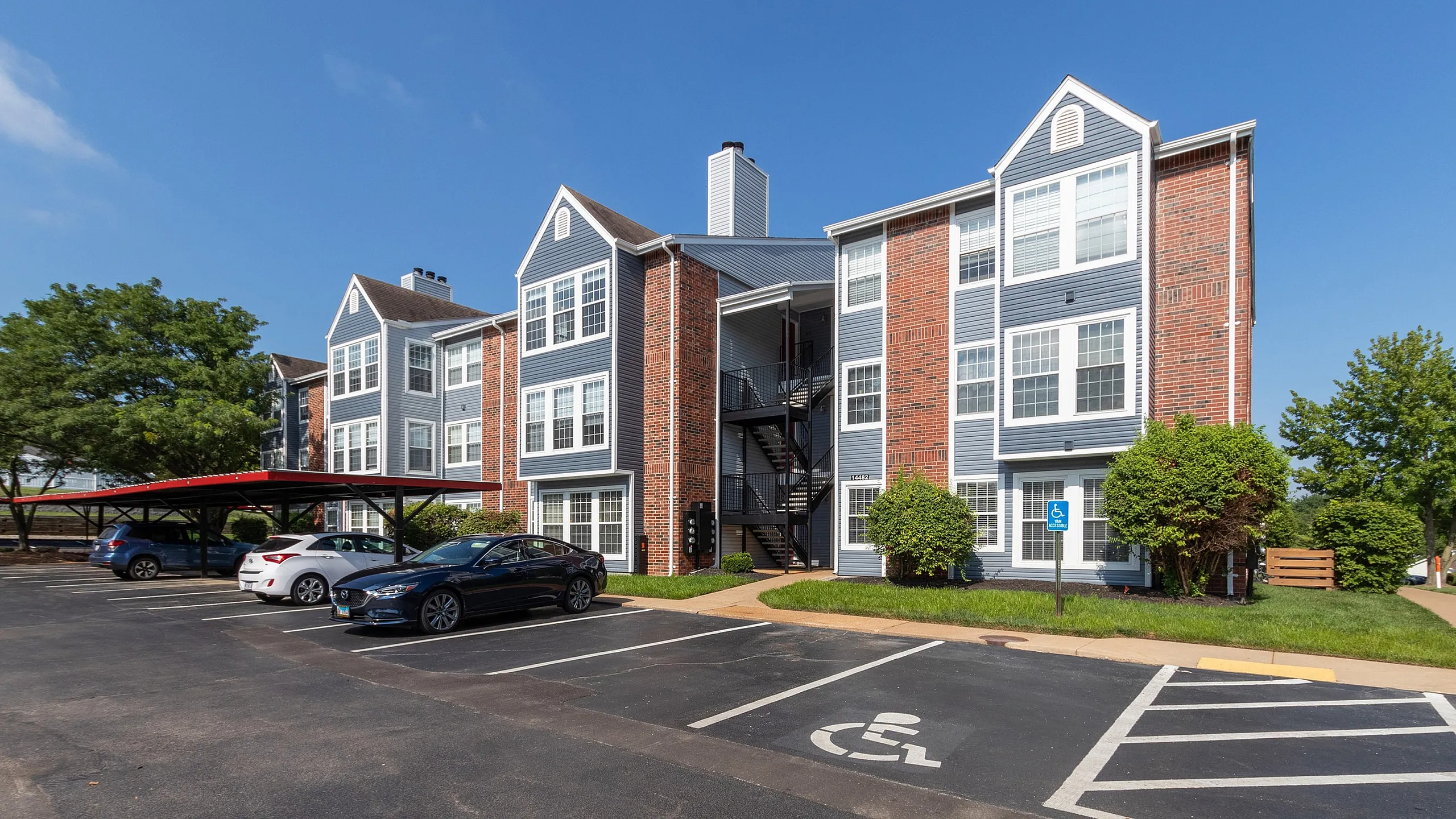 Charming three-story apartment complex with modern brick facade, surrounded by lush greenery and convenient covered parking.