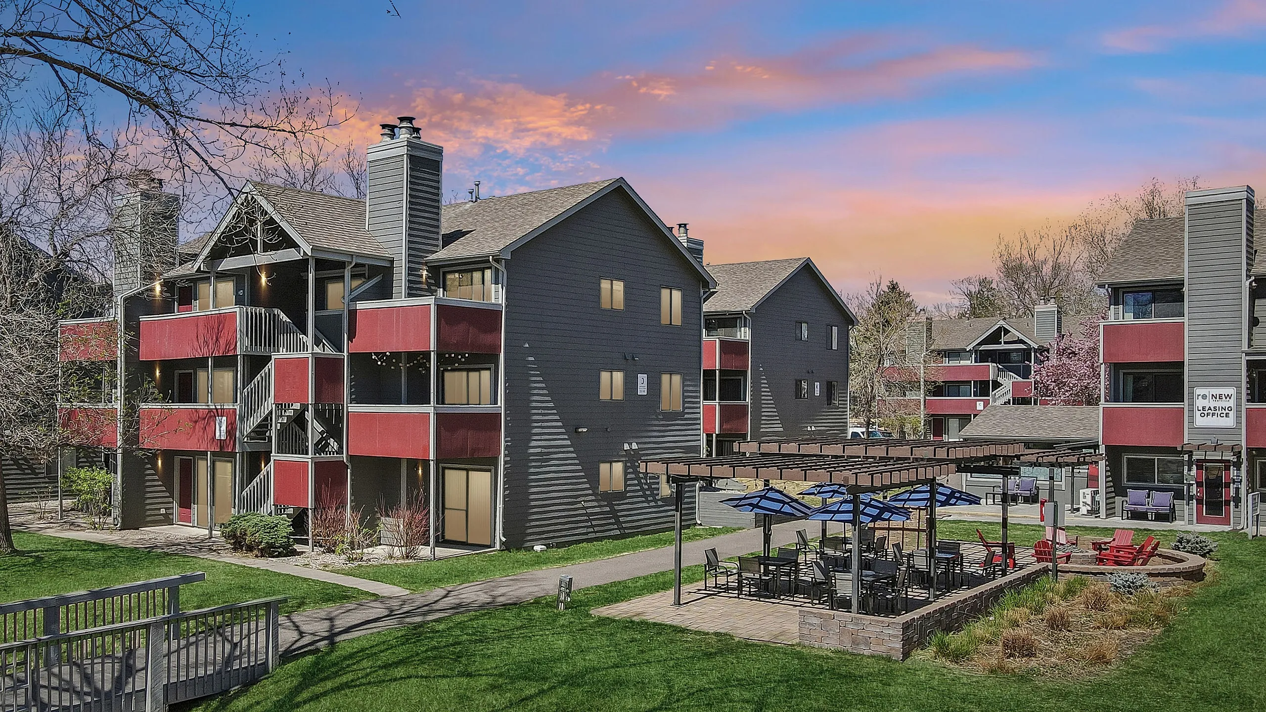 Charming apartment complex at sunset with modern architecture, vibrant red accents, and inviting outdoor seating areas.