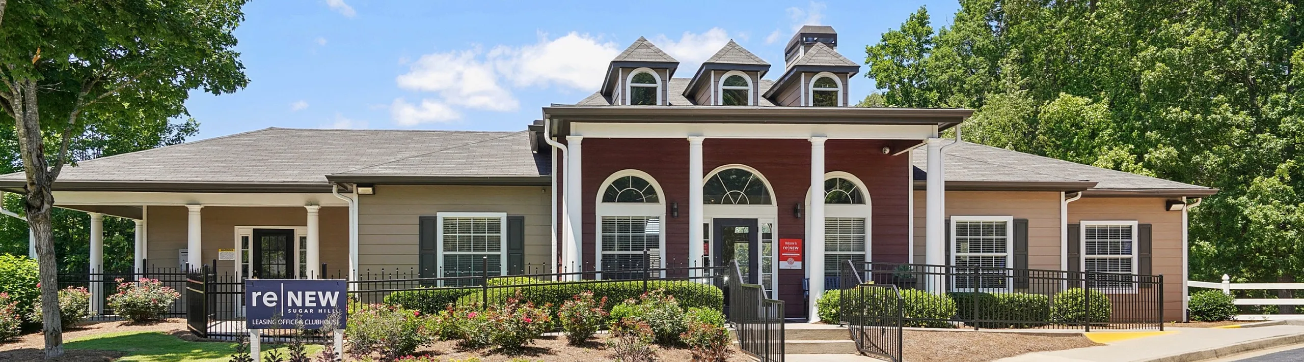 Charming community leasing office with classic architecture, surrounded by lush greenery and vibrant gardens.