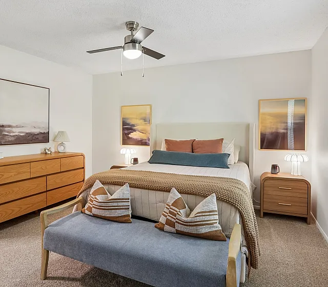 Inviting bedroom with modern decor, featuring a cozy bed, stylish dresser, and scenic artwork, bathed in natural light.