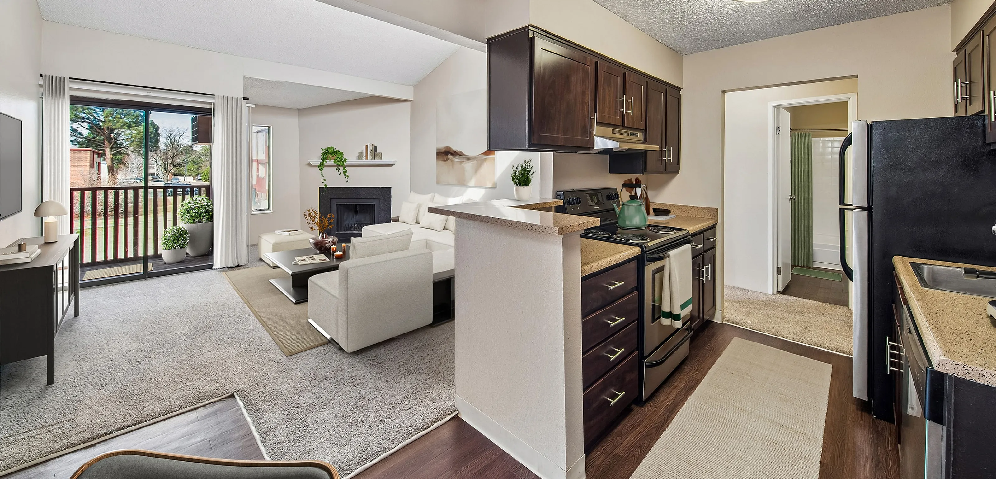 Chic open-concept apartment with modern kitchen, inviting living area with fireplace, and large sliding doors to balcony with lush view.
