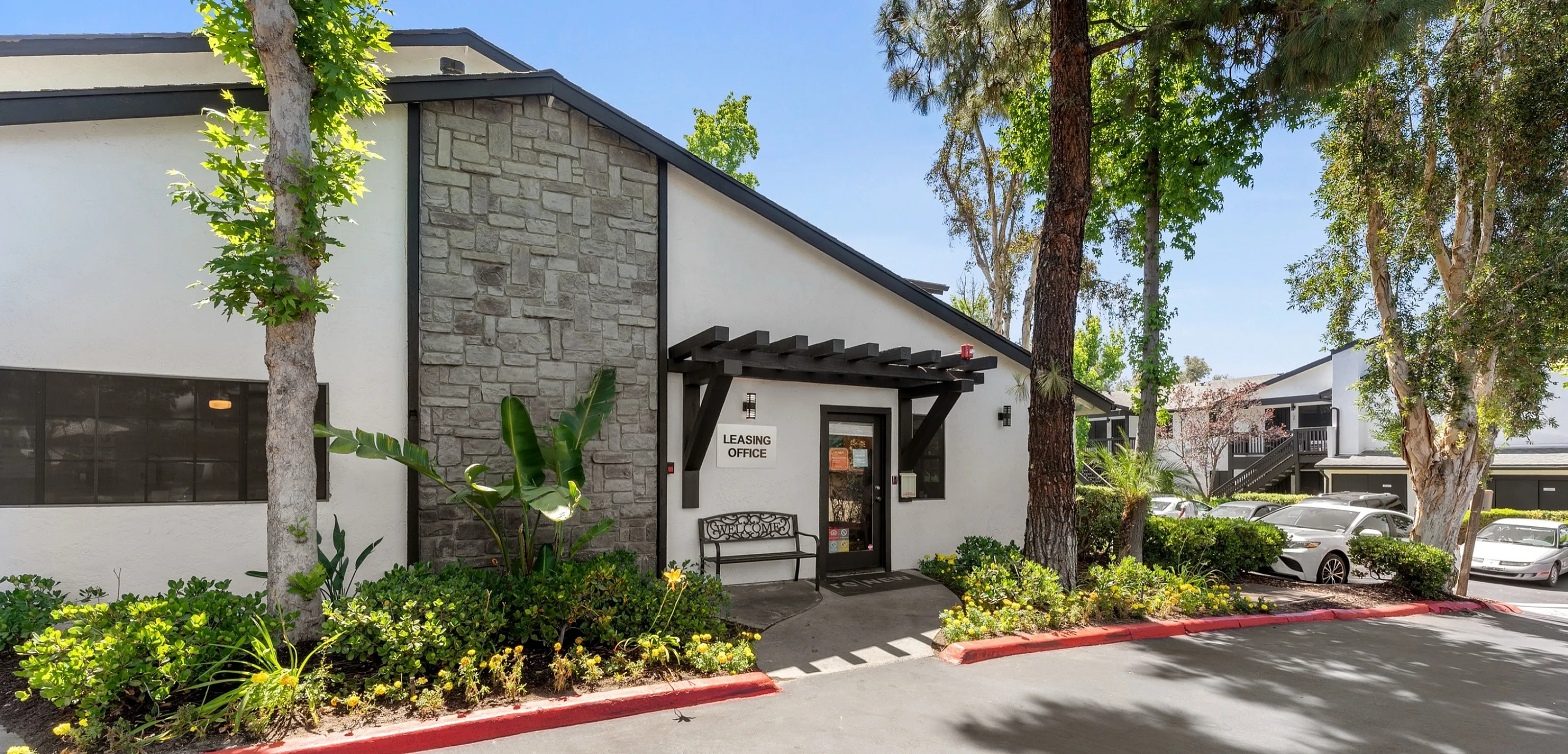 Inviting leasing office exterior surrounded by lush greenery and modern architectural design.