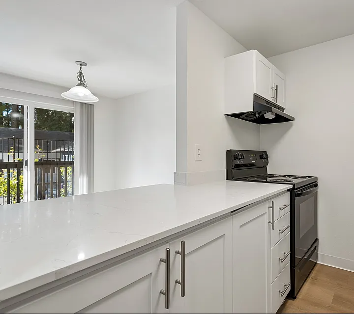 Modern kitchen with sleek white cabinetry, elegant marble countertops, and high-quality black appliances opening to a sunlit balcony.