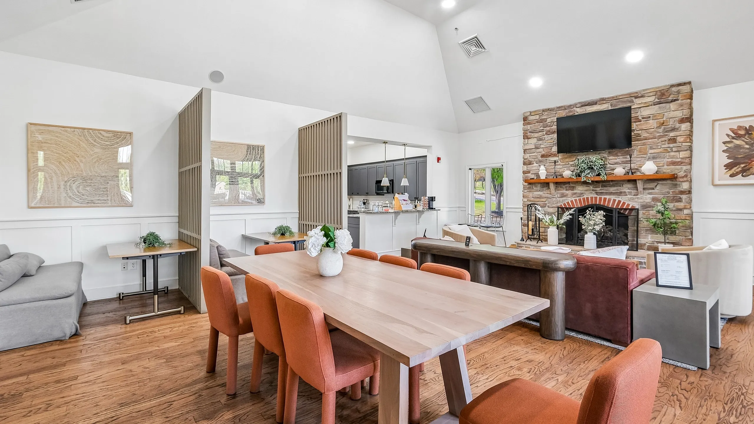 Contemporary open-concept living space featuring elegant dining area with orange chairs, cozy lounge with stone fireplace, and modern kitchen, ideal for hosting and relaxation.