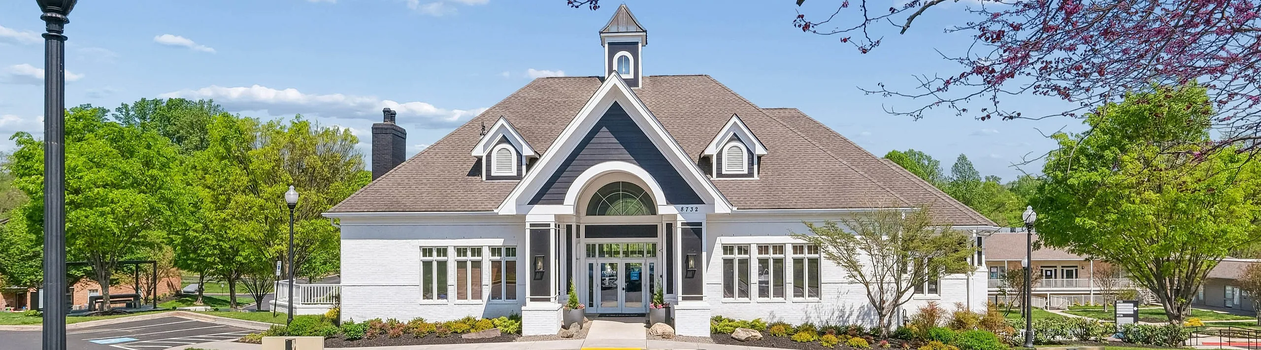 Charming community clubhouse with classic architecture, surrounded by lush greenery and vibrant spring blossoms in a welcoming neighborhood setting.