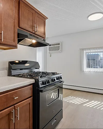 Modern kitchen with wooden cabinets, sleek black appliances, and abundant natural light from a large window, creating a warm and inviting space.
