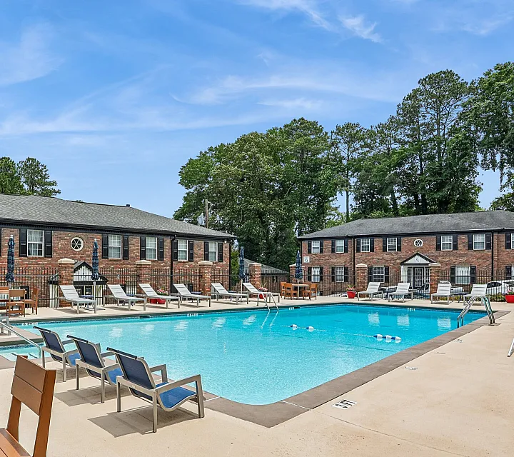 Charming outdoor pool area with lounging chairs, surrounded by classic brick apartments under a clear blue sky.