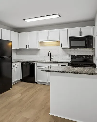 Chic, modern kitchen with sleek black appliances, granite countertops, and elegant white cabinetry, featuring an open layout with beautiful wood flooring.