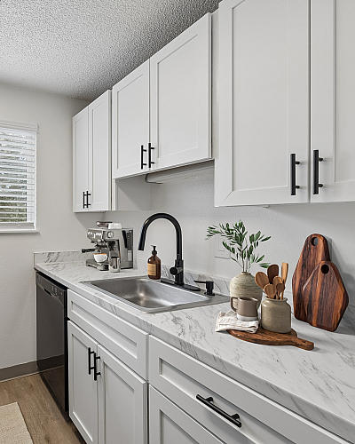 Modern kitchen with sleek white cabinets, marble countertops, and natural light streaming through a large window.