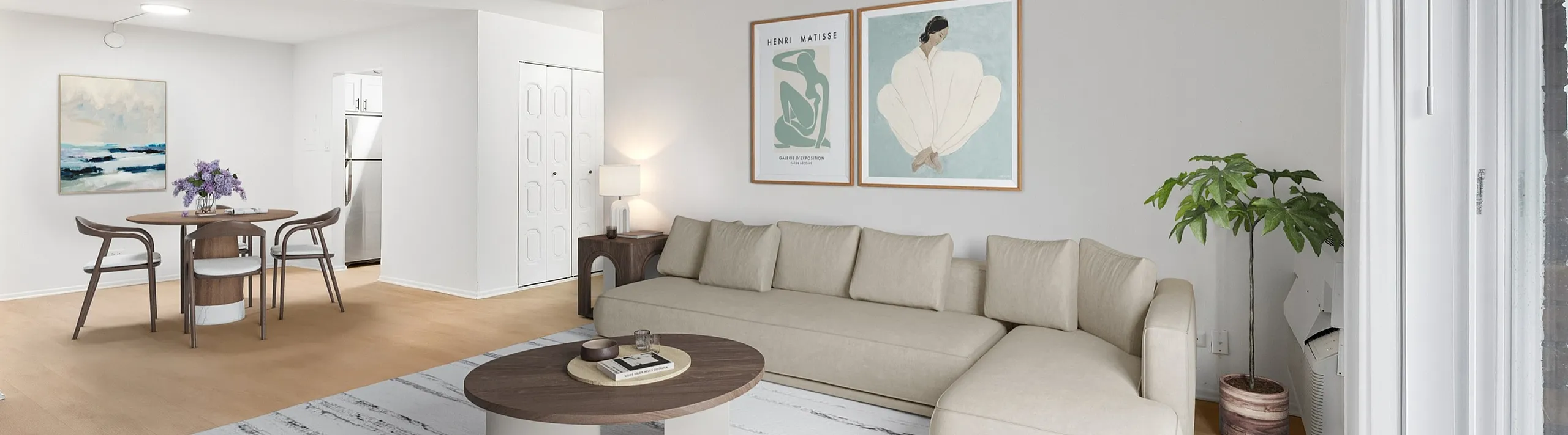 Modern open-concept living room with stylish decor, featuring a plush beige sectional, chic round dining table, and vibrant artwork. Abundant natural light streams through large windows, offering a cozy and inviting atmosphere.