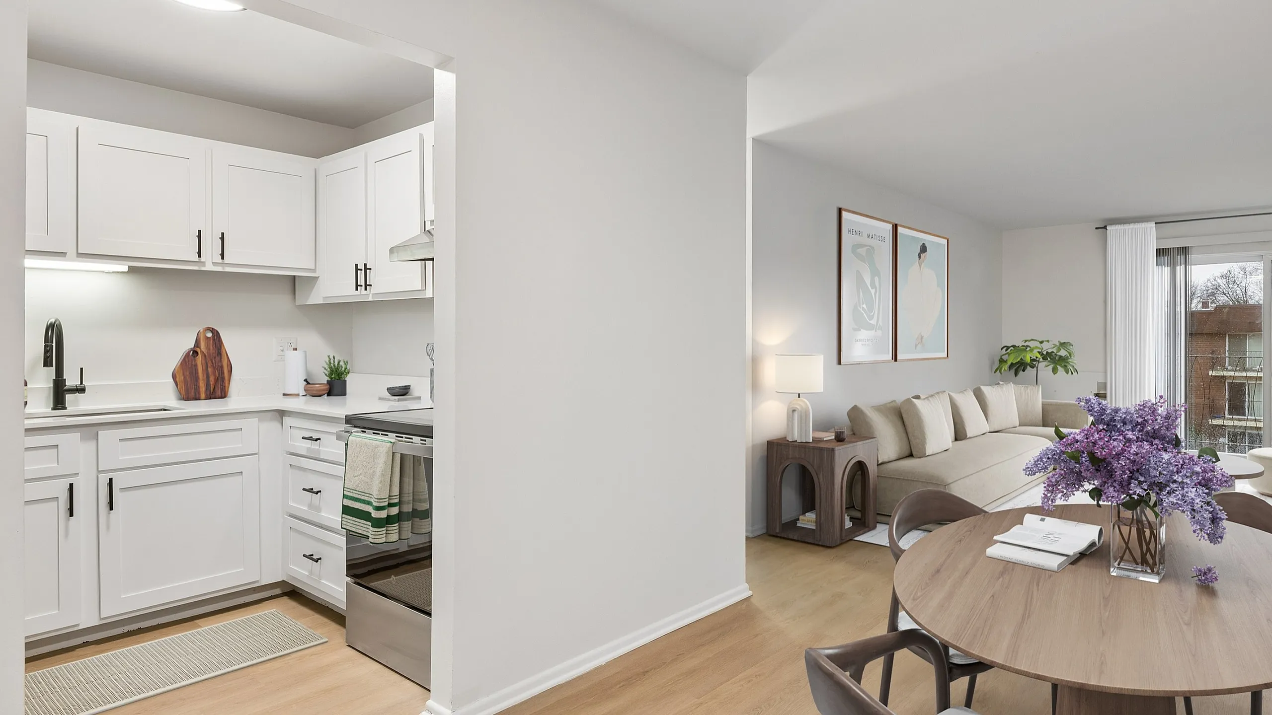 Modern open-concept living space featuring a stylish kitchen with white cabinetry, cozy living room, and elegant dining area adorned with fresh flowers.