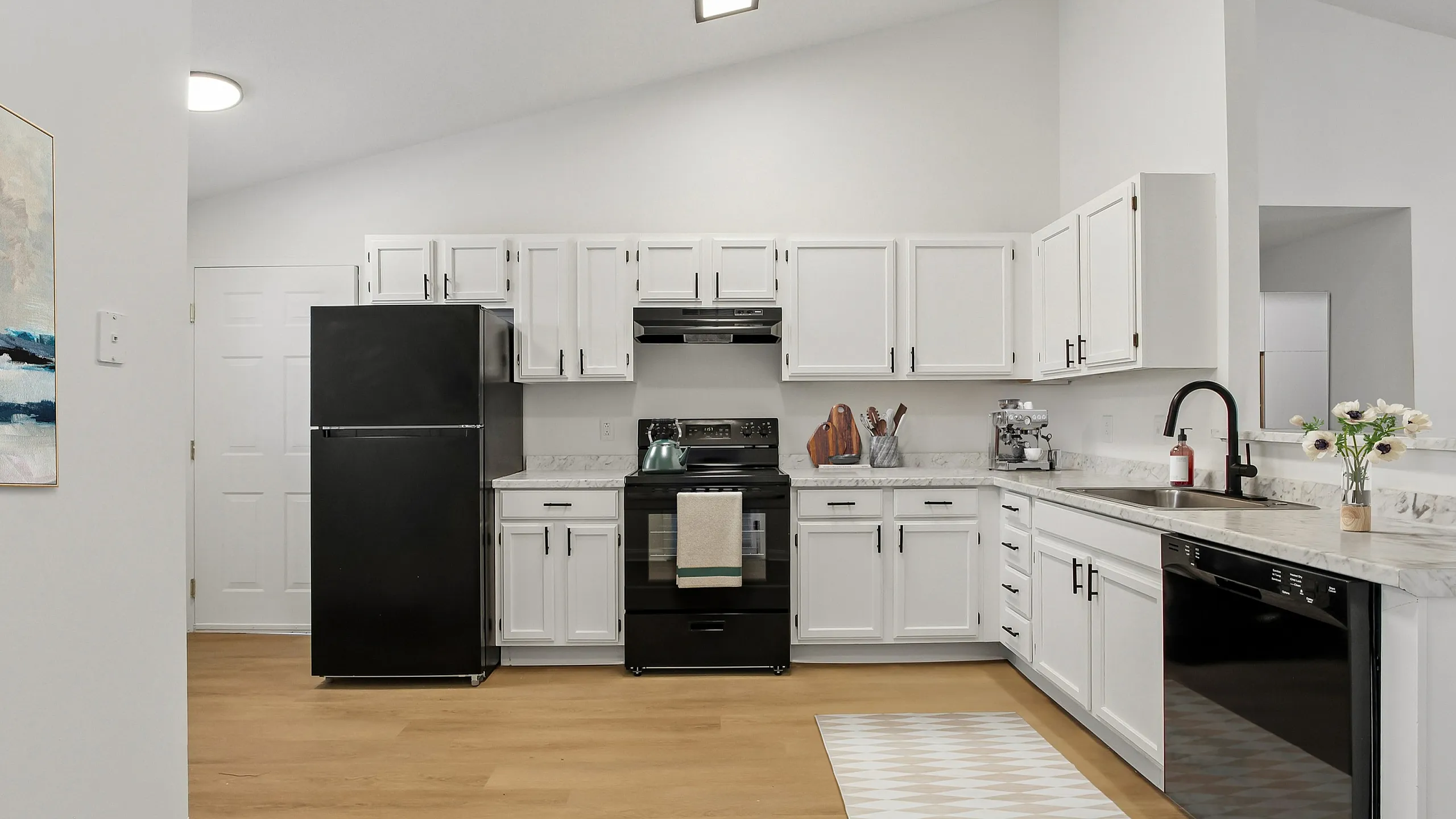 Bright and modern kitchen with sleek black appliances, elegant white cabinetry, and stylish marble countertops offering a perfect blend of functionality and design.