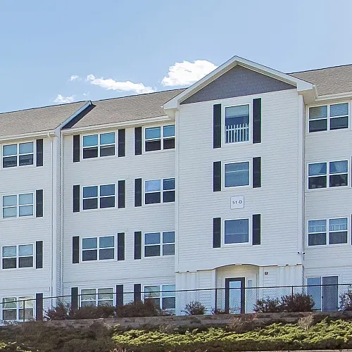 Charming residential complex with elegant multi-story buildings, beautifully integrated into a serene landscape, under a radiant blue sky.