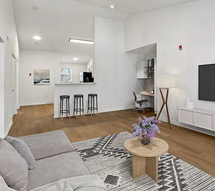 Modern apartment living room featuring elegant hardwood floors, stylish decor, a cozy sofa, and a bright open-plan kitchen with sleek bar stools.