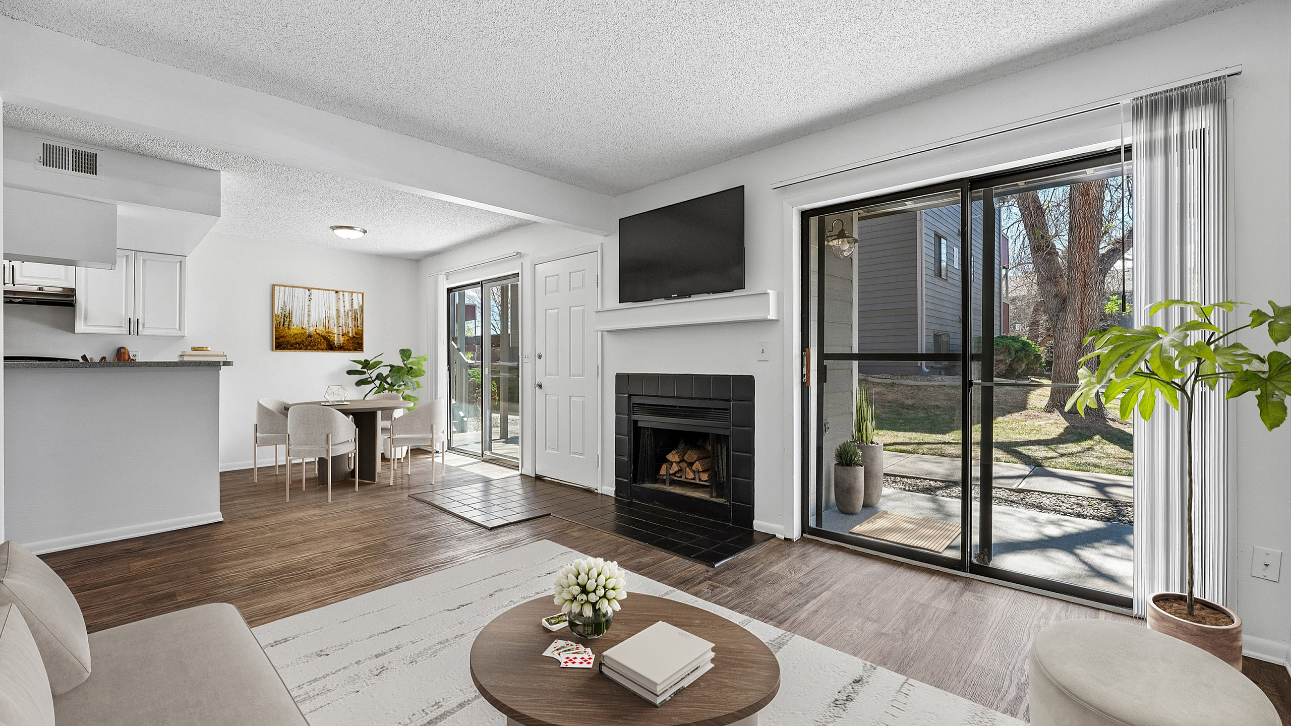 Bright and inviting living space featuring a cozy fireplace, modern decor, and large sliding glass doors opening to a lush outdoor view.