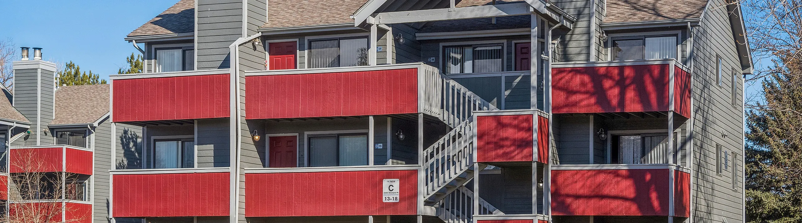 Charming apartment building with bold red balconies and inviting red doors, nestled in a serene neighborhood with vibrant greenery.