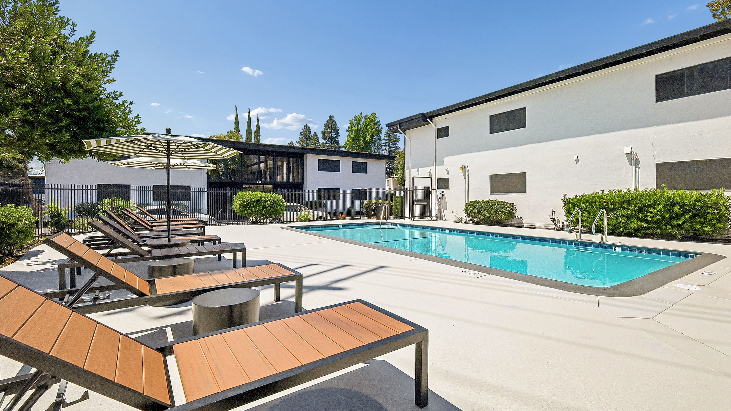 Luxurious outdoor area featuring a sparkling swimming pool, stylish sun loungers, and lush landscaping under a clear blue sky.