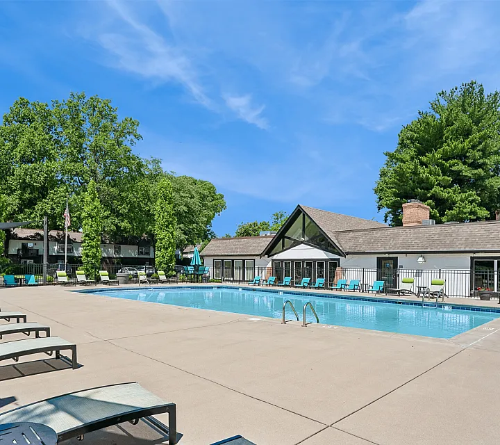 Inviting outdoor pool area with modern lounge chairs, surrounded by lush greenery and a blue sky.