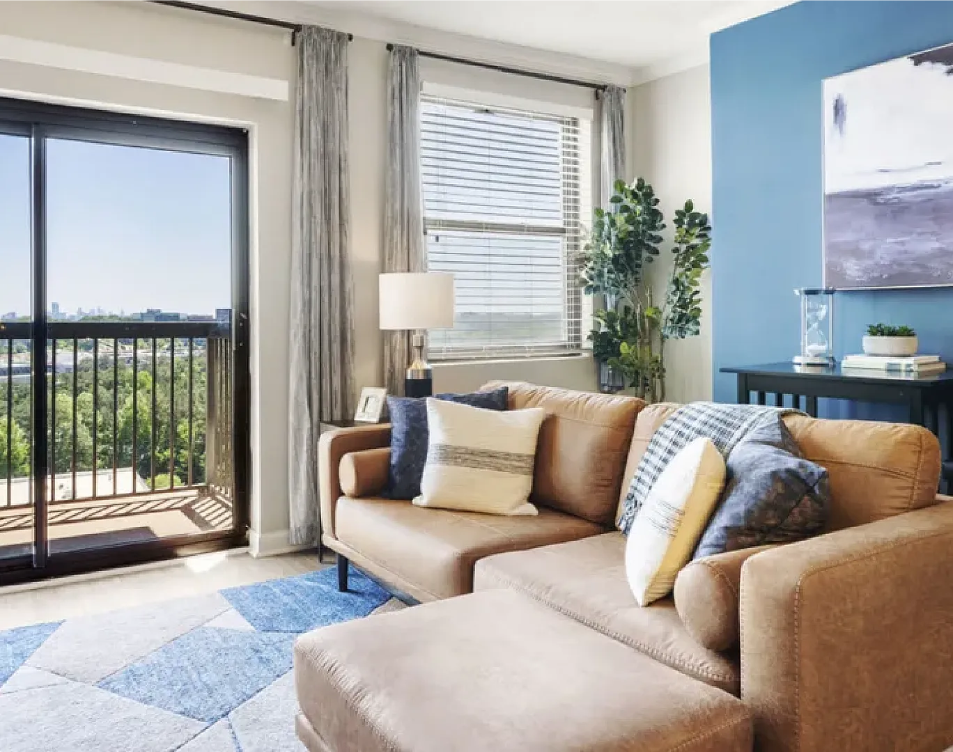 Bright, cozy living room with modern decor, featuring a plush tan sofa, chic blue accent wall, and large windows offering stunning city views.