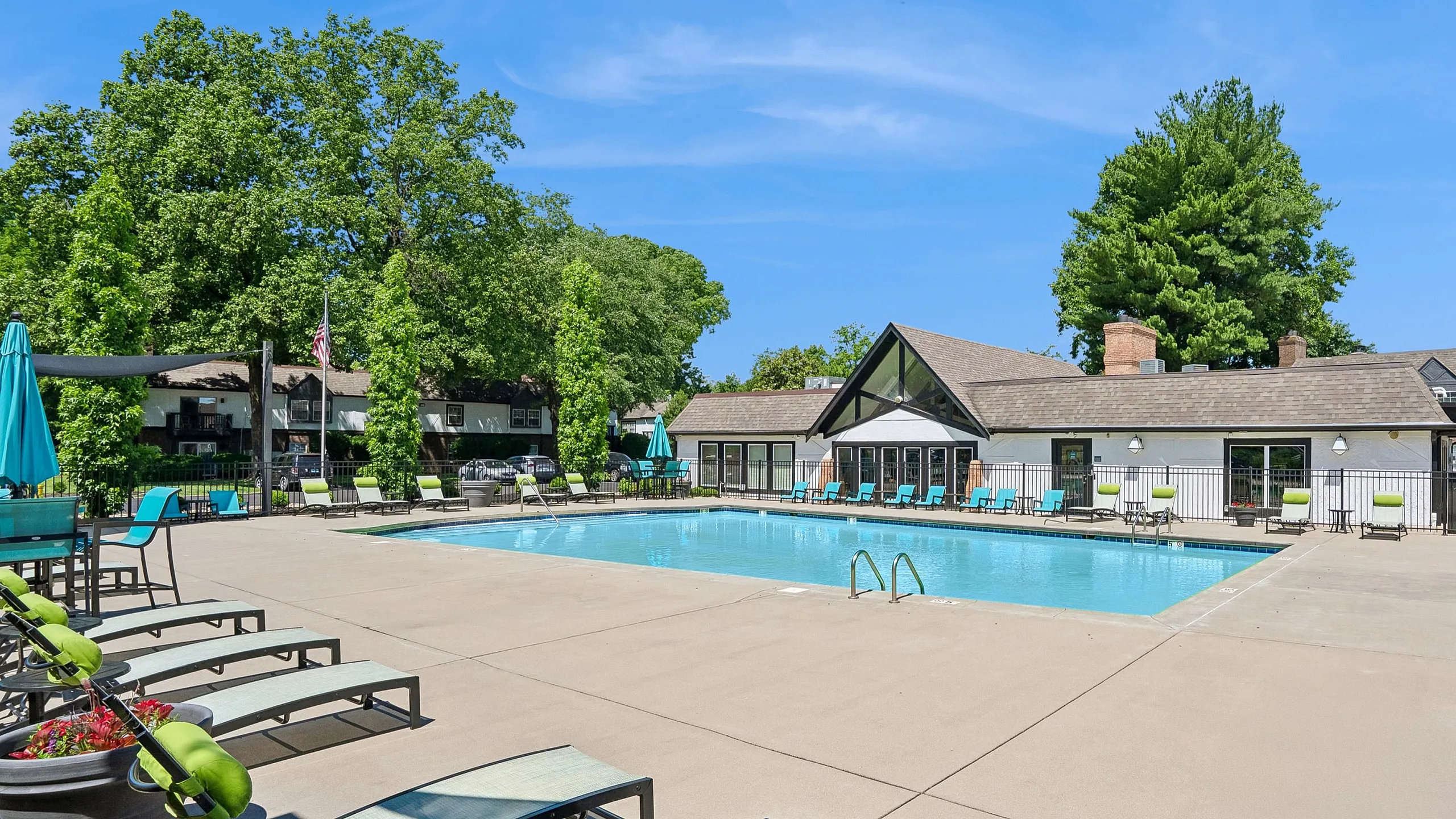 Inviting outdoor swimming pool area surrounded by comfortable lounge chairs and lush green trees, under a bright blue sky.