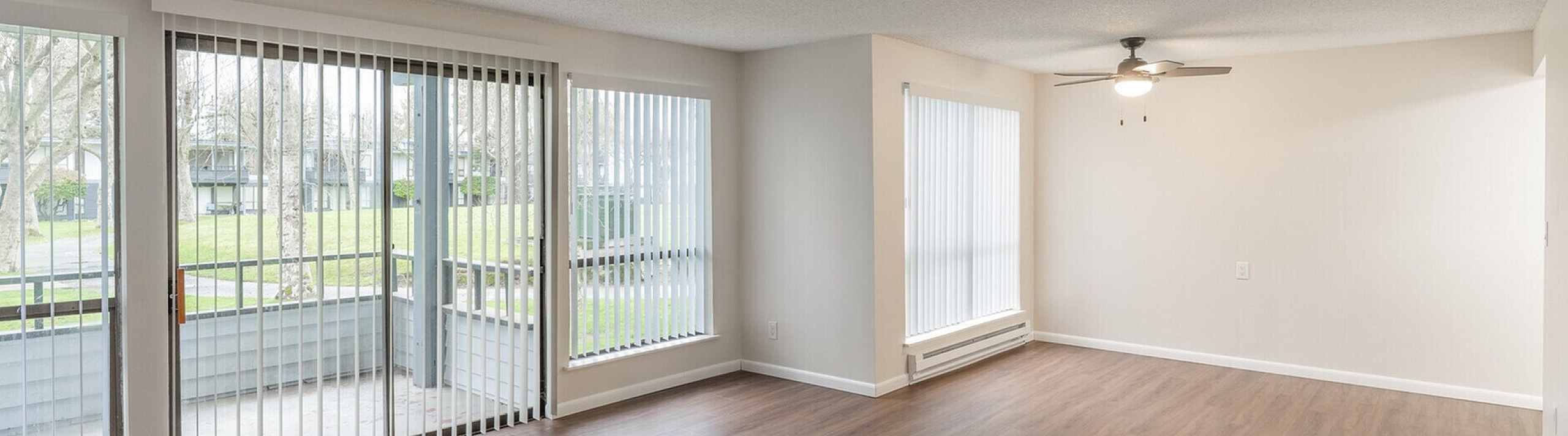 Bright and spacious open-concept living room with large windows overlooking greenery, featuring elegant wooden flooring and a modern ceiling fan.