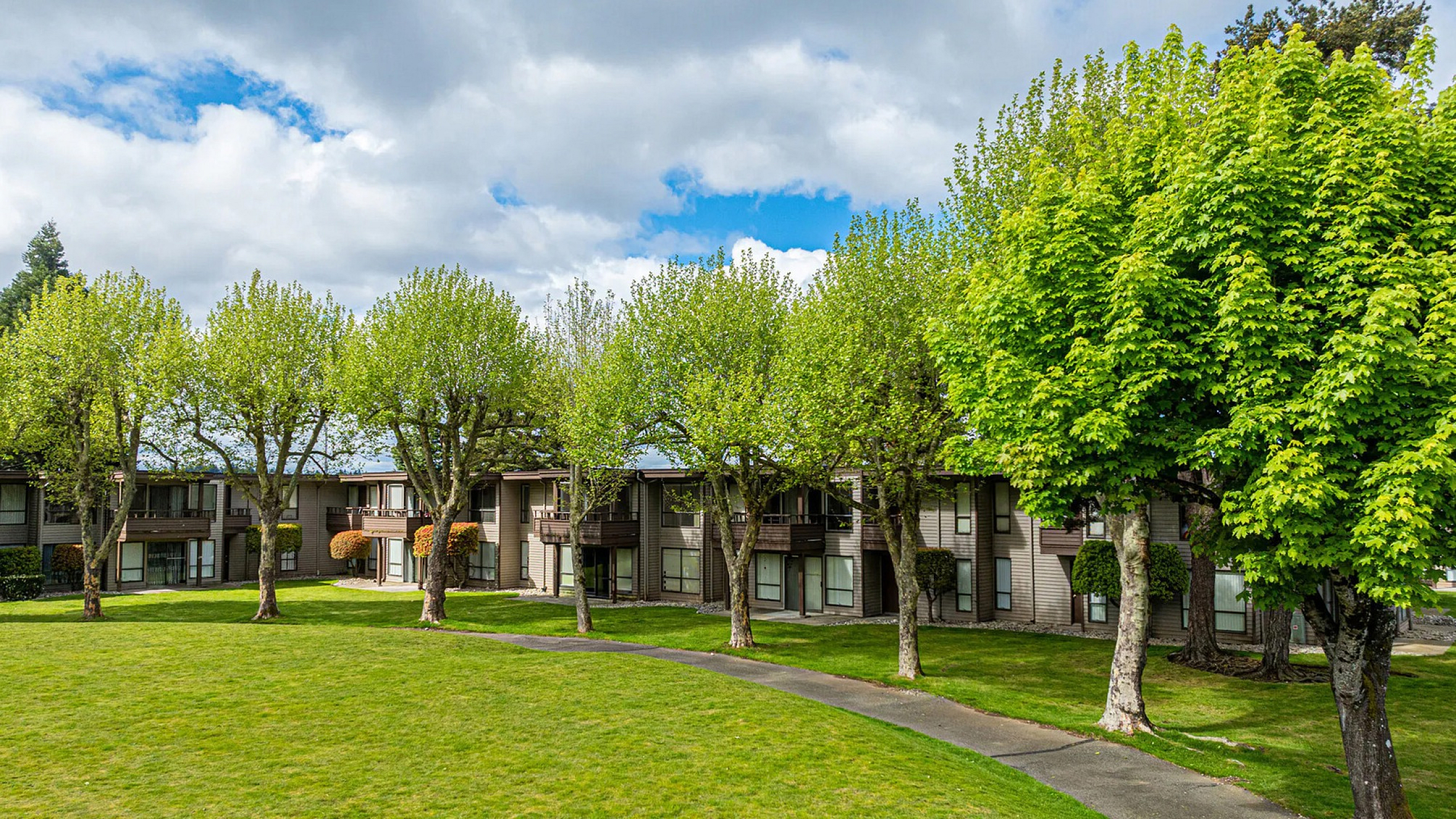 Charming apartment complex surrounded by lush greenery and mature trees, offering a serene and inviting atmosphere.