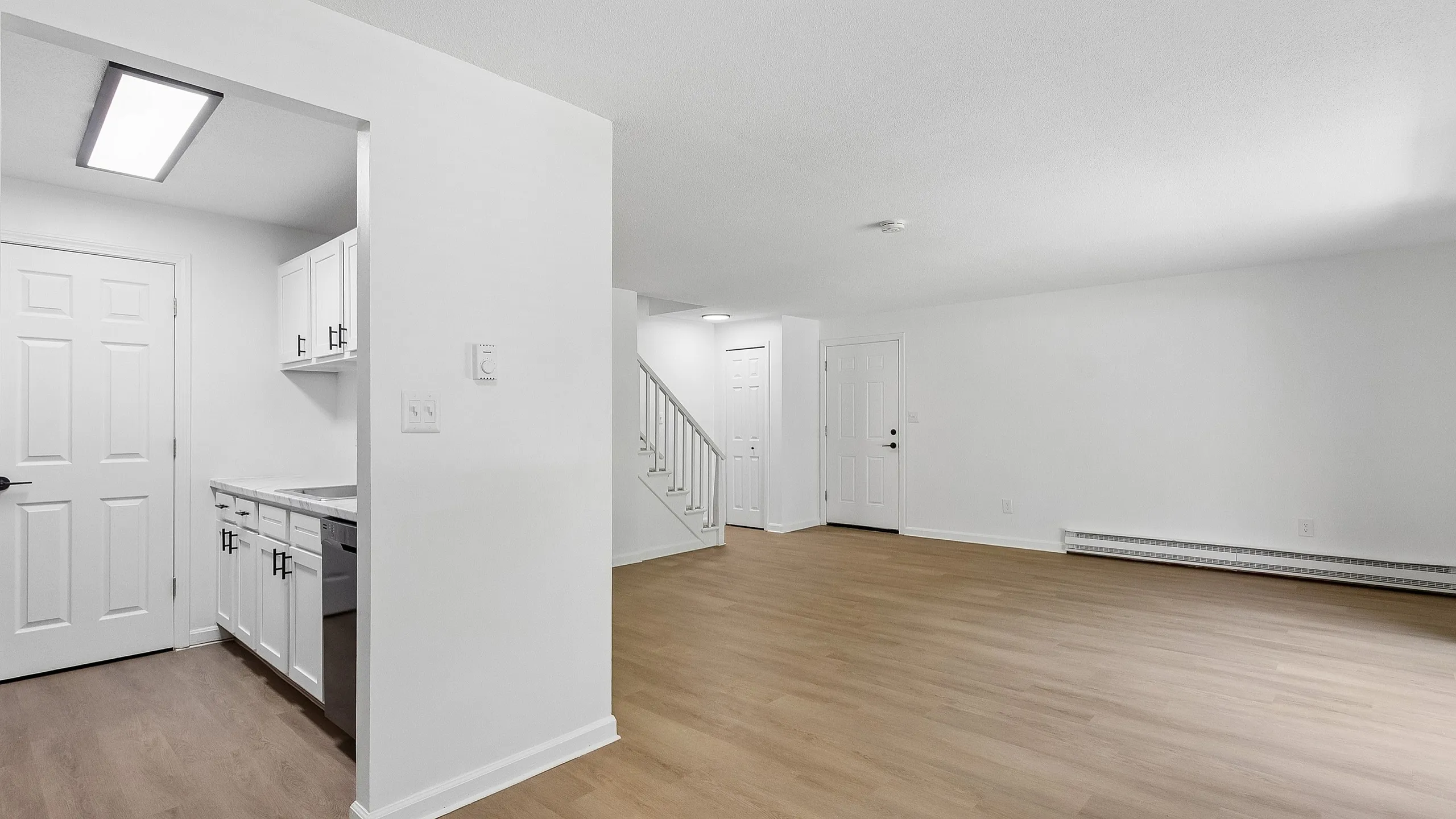 Modern open-concept living space with sleek wooden flooring, pristine white walls, and a bright, inviting kitchen area.