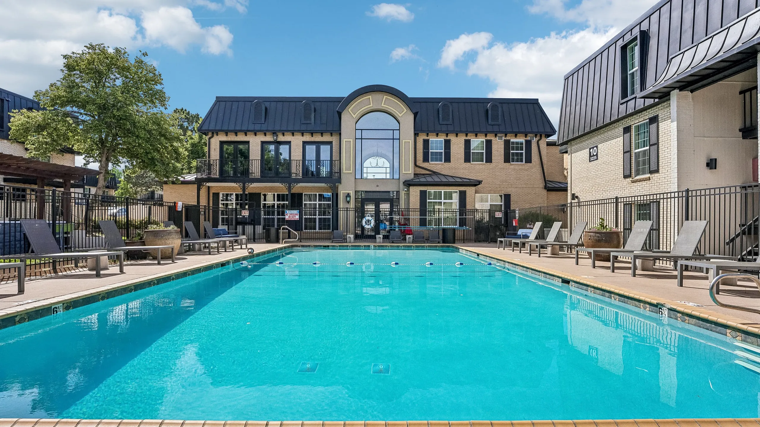Inviting apartment community featuring a sparkling outdoor pool with modern lounge chairs, framed by elegant architecture and lush greenery.