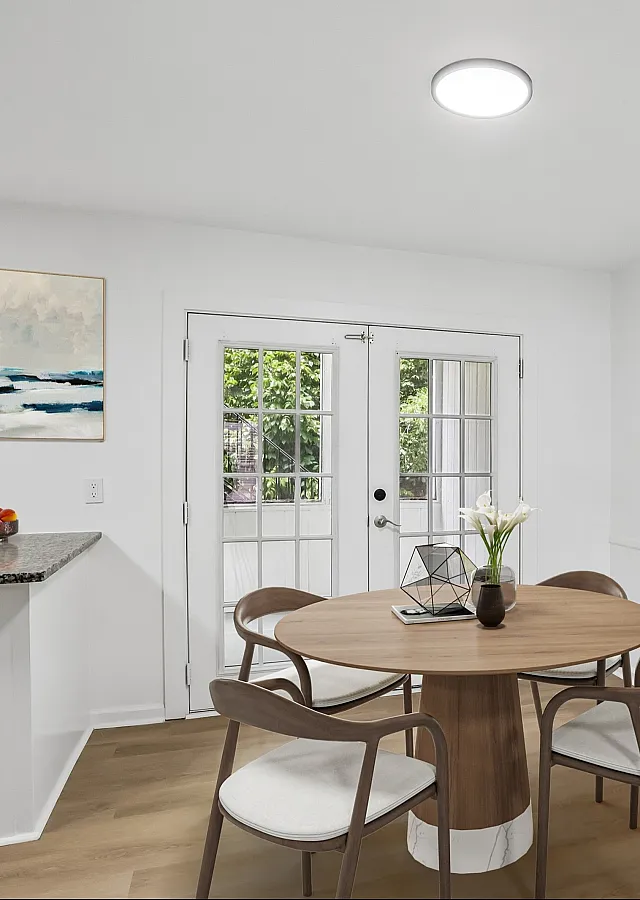 Contemporary dining area with elegant round wooden table, stylish chairs, and vibrant artwork, adjacent to bright French doors.