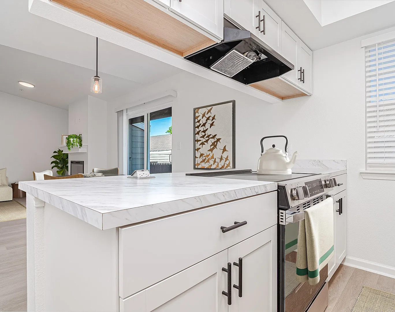 Modern kitchen with sleek marble countertops adjacent to a cozy living area with natural light pouring through large windows.