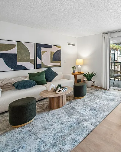 Modern living room with elegant decor, featuring a cozy sofa, stylish artwork, and a large window leading to a balcony with outdoor views.