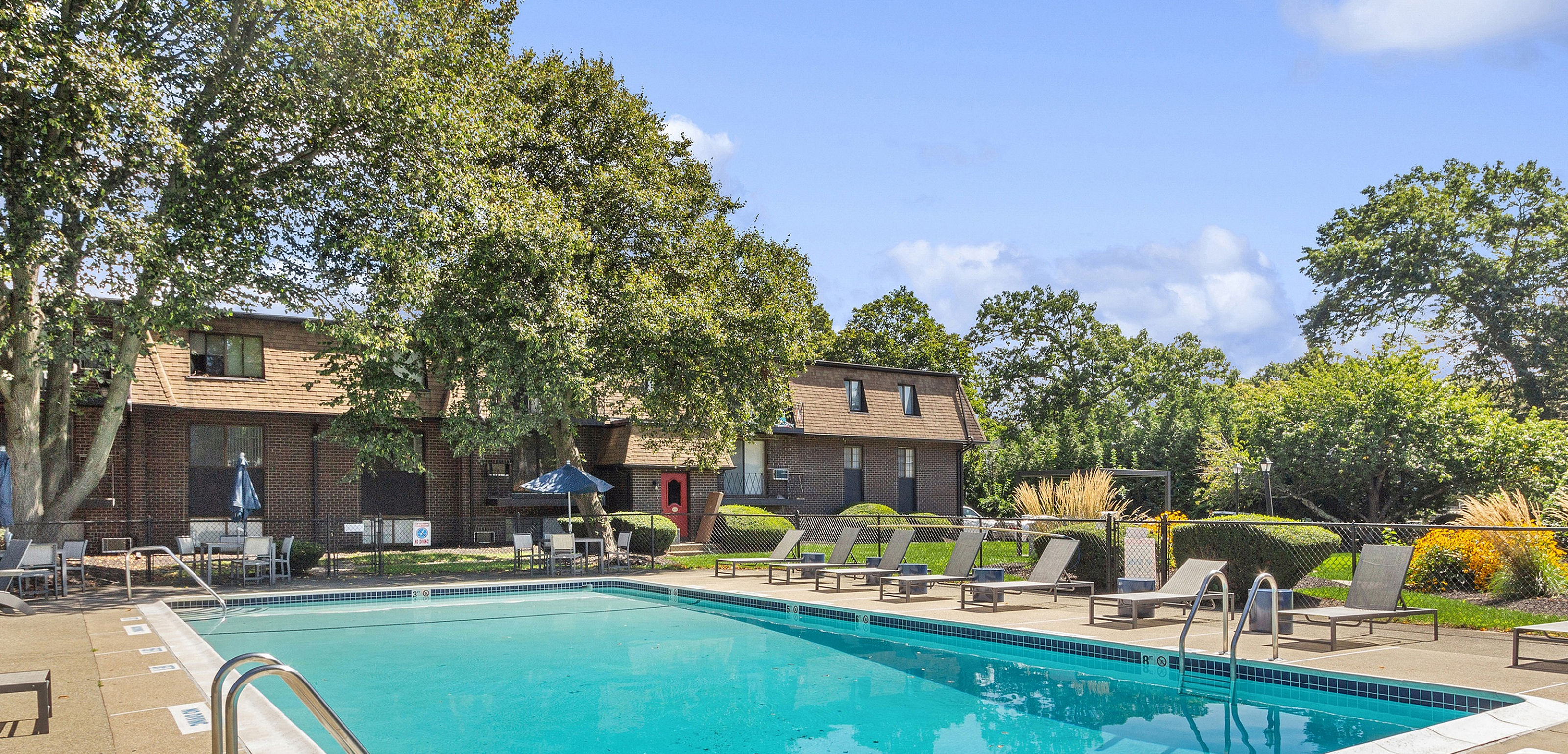 Inviting outdoor pool area with comfortable loungers surrounded by lush greenery and stylish apartment buildings.