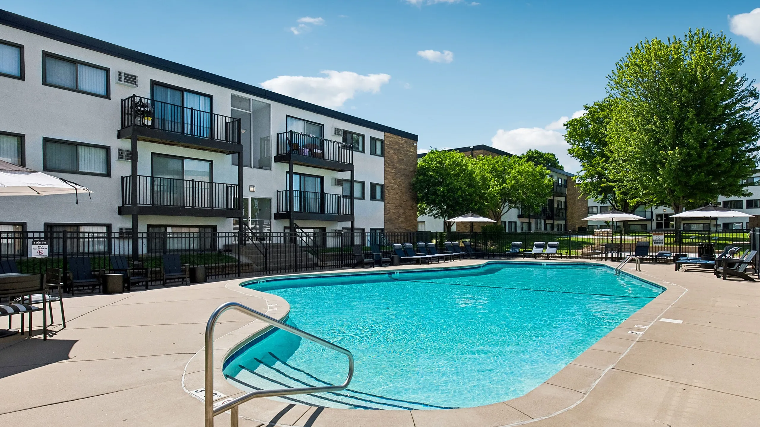 Charming apartment complex featuring a sunlit swimming pool, inviting relaxation area, and modern balconies.