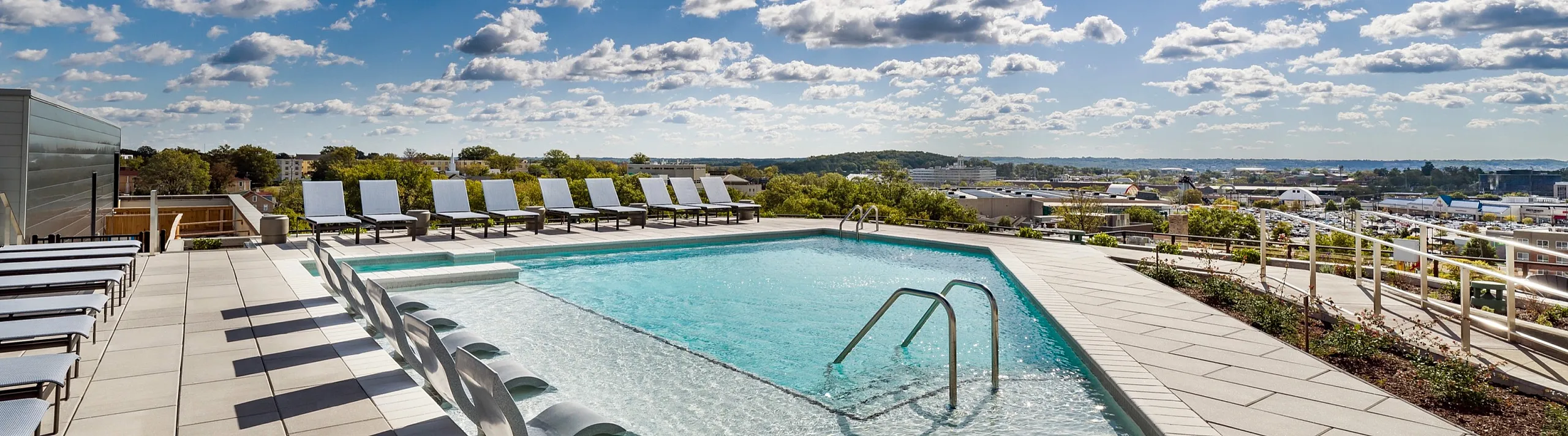 Breathtaking rooftop pool with panoramic city views, luxurious lounge chairs, and a bright blue sky, perfect for relaxation and leisure.