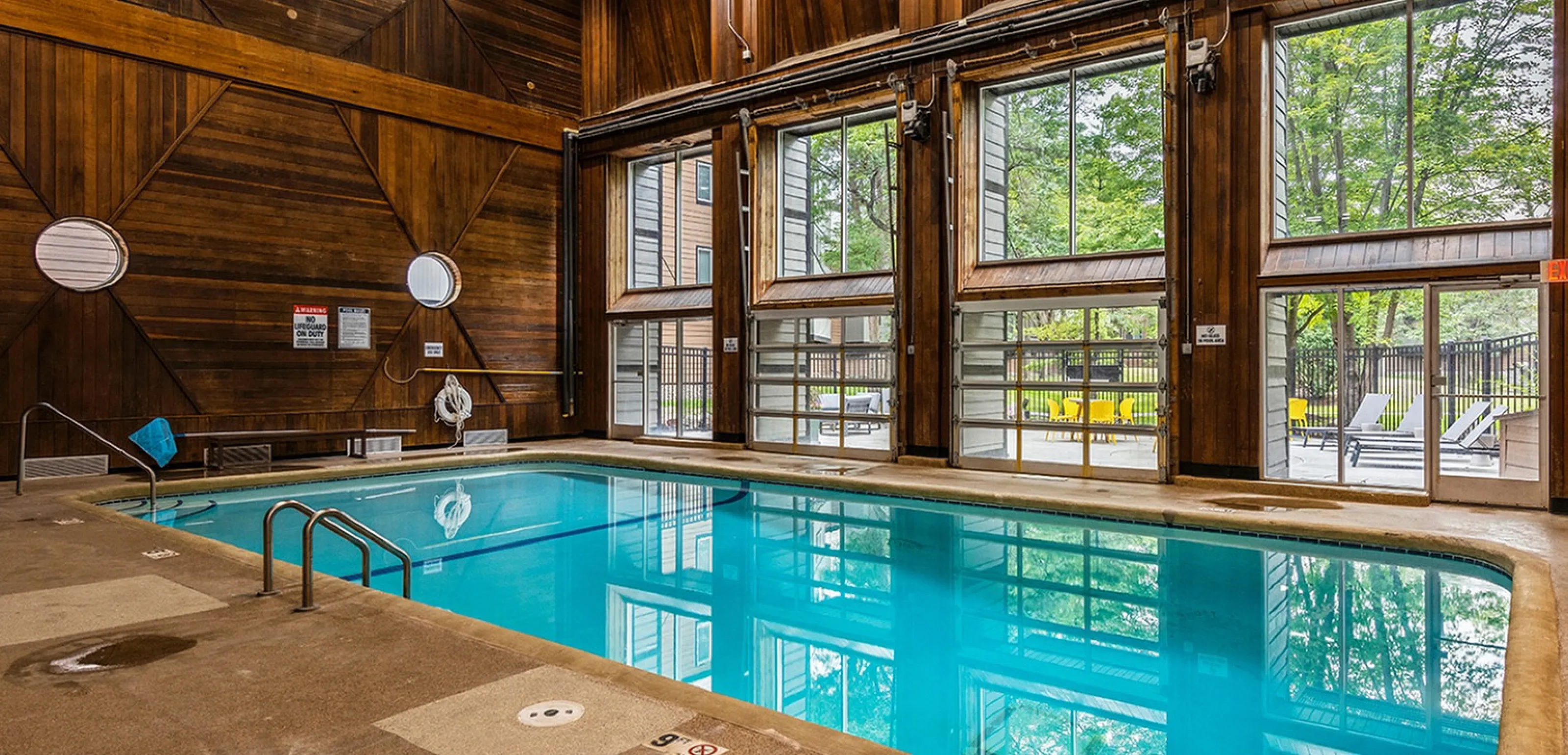 Luxurious indoor pool with elegant wood-paneled walls and large windows offering scenic outdoor views.