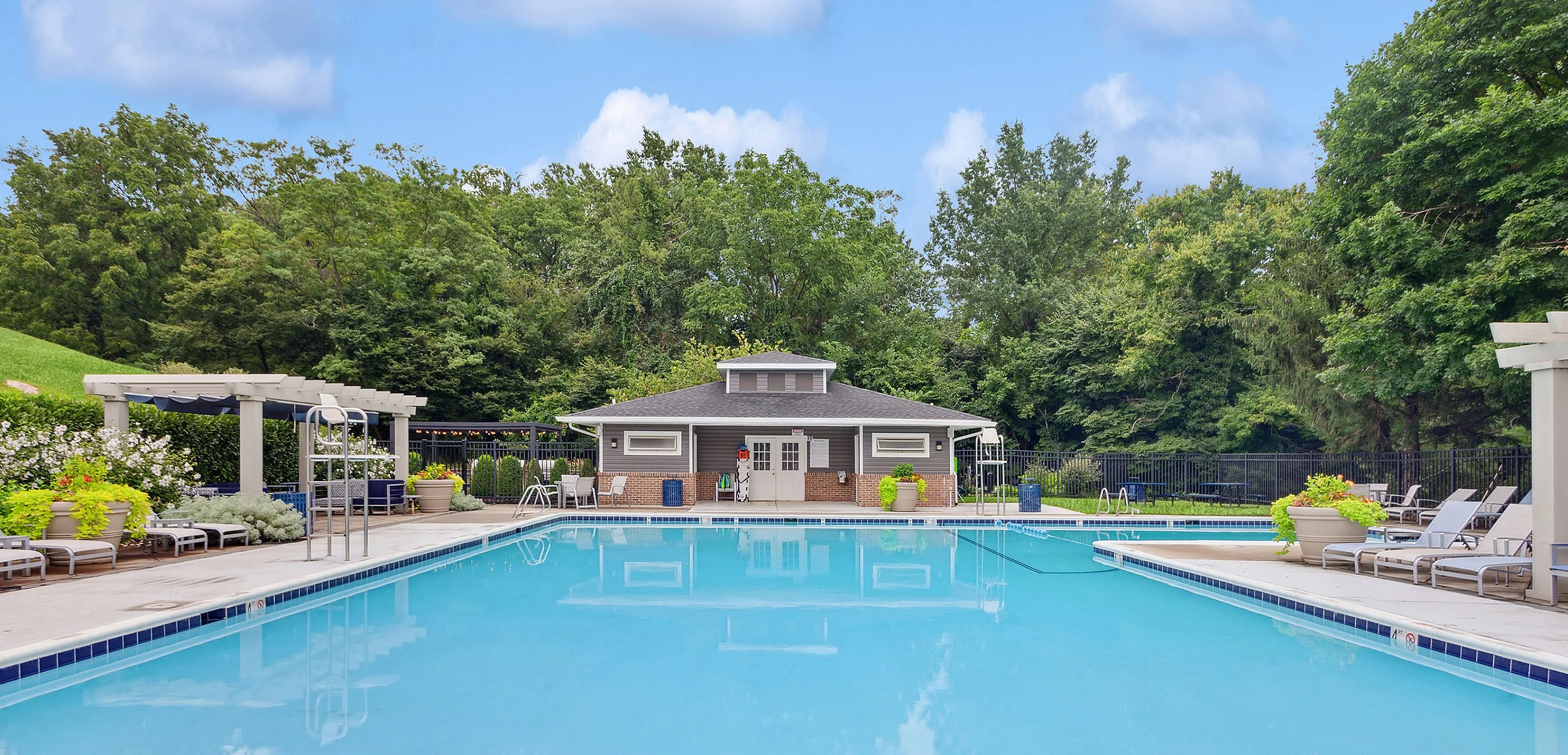 Inviting outdoor pool area with luxurious lounge seating and lush greenery, perfect for relaxation.