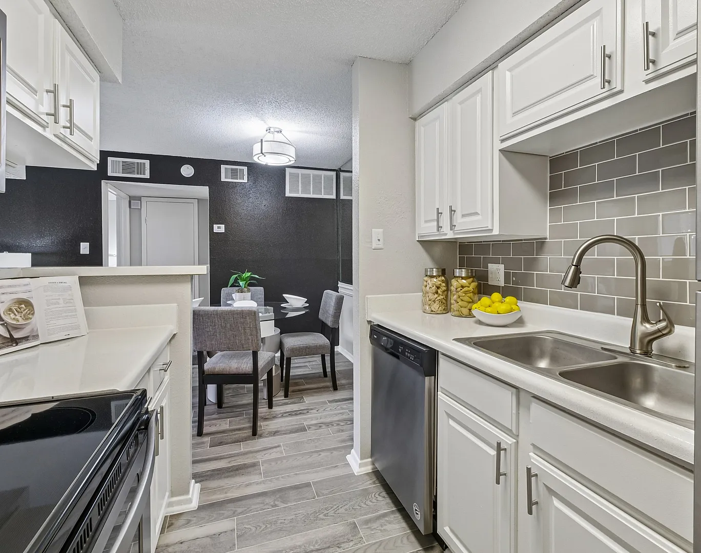 Modern apartment kitchen with sleek white cabinetry, stainless steel appliances, and a cozy dining area in the background.