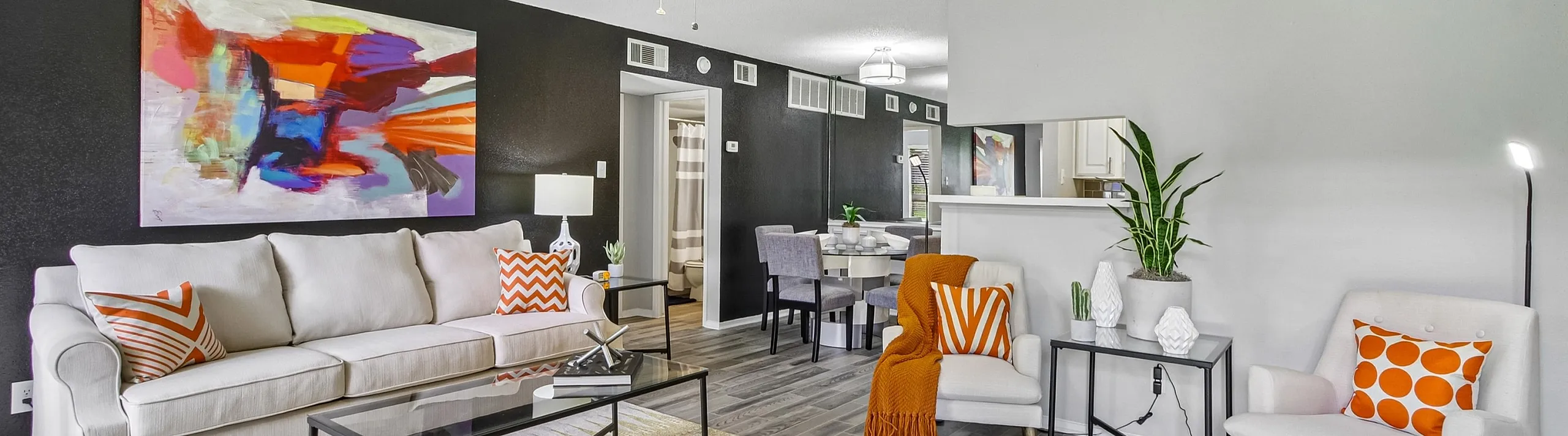 Bright modern living room with stylish gray flooring, vibrant abstract art, and cozy seating accented by colorful cushions.