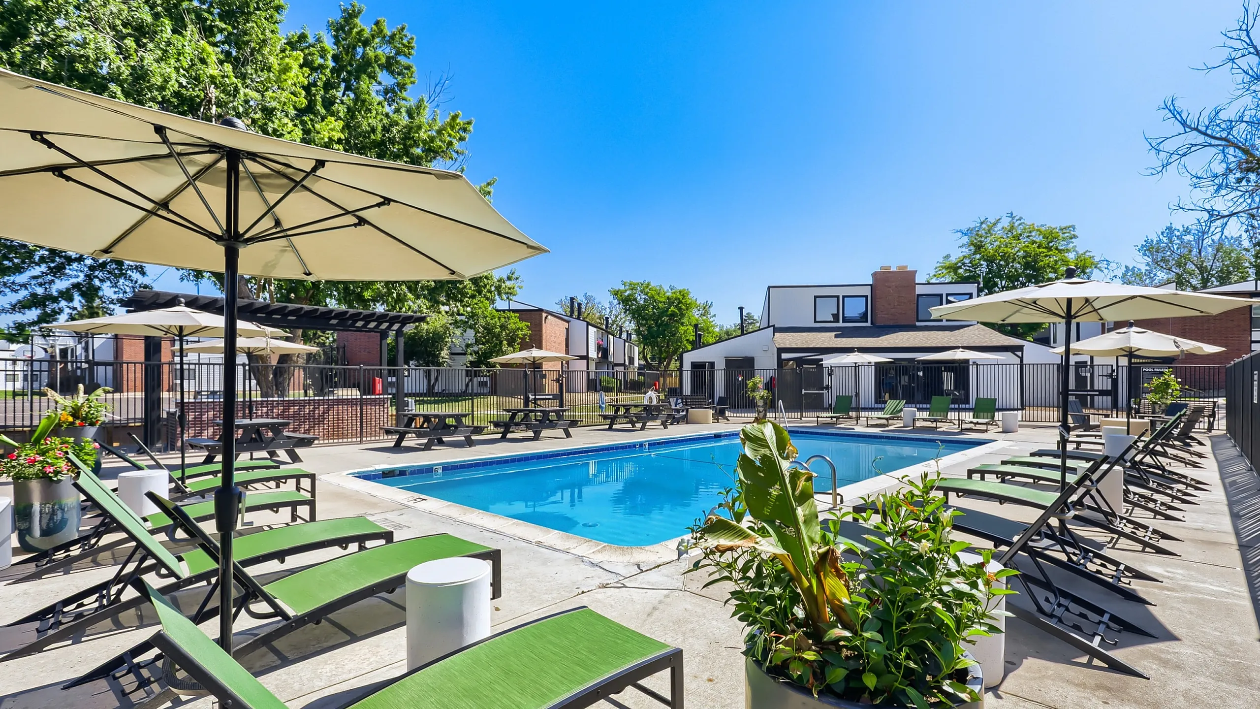 Charming outdoor pool area with vibrant green lounge chairs, elegant umbrellas, and lush greenery, offering a serene retreat for relaxation and leisure.
