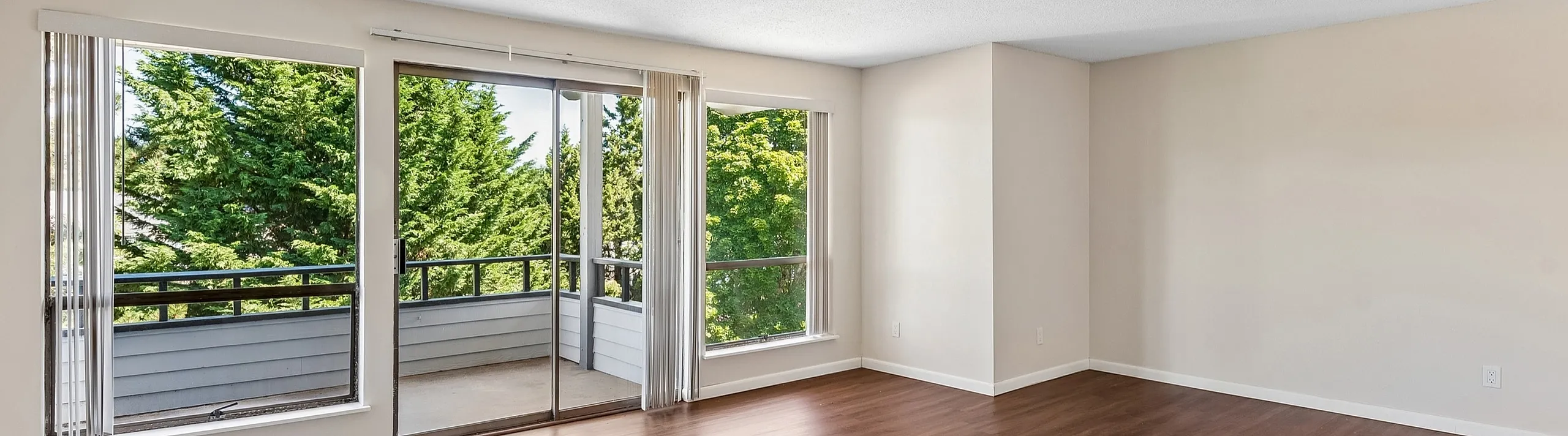 Bright and airy living room with large windows offering picturesque views of lush greenery, complemented by elegant hardwood floors.