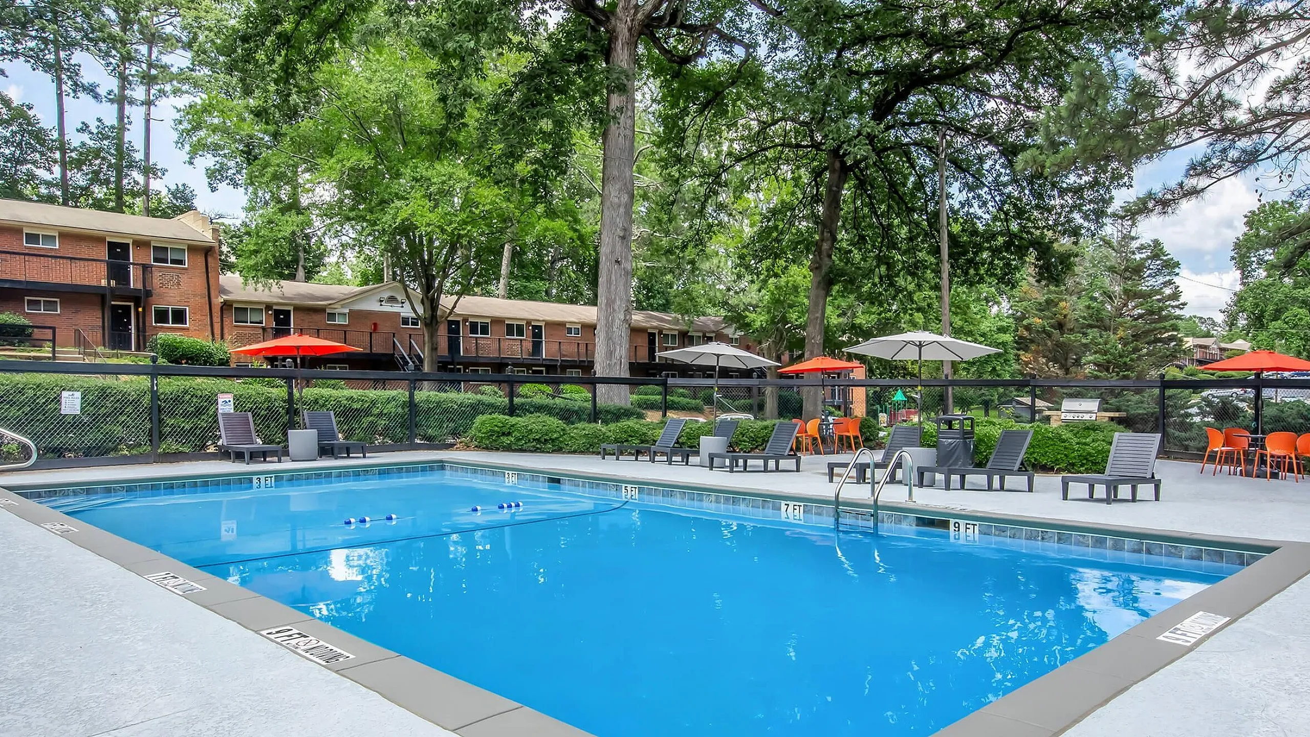 Inviting outdoor pool area with sun loungers, vibrant orange umbrellas, and lush greenery, perfect for relaxation and social gatherings.