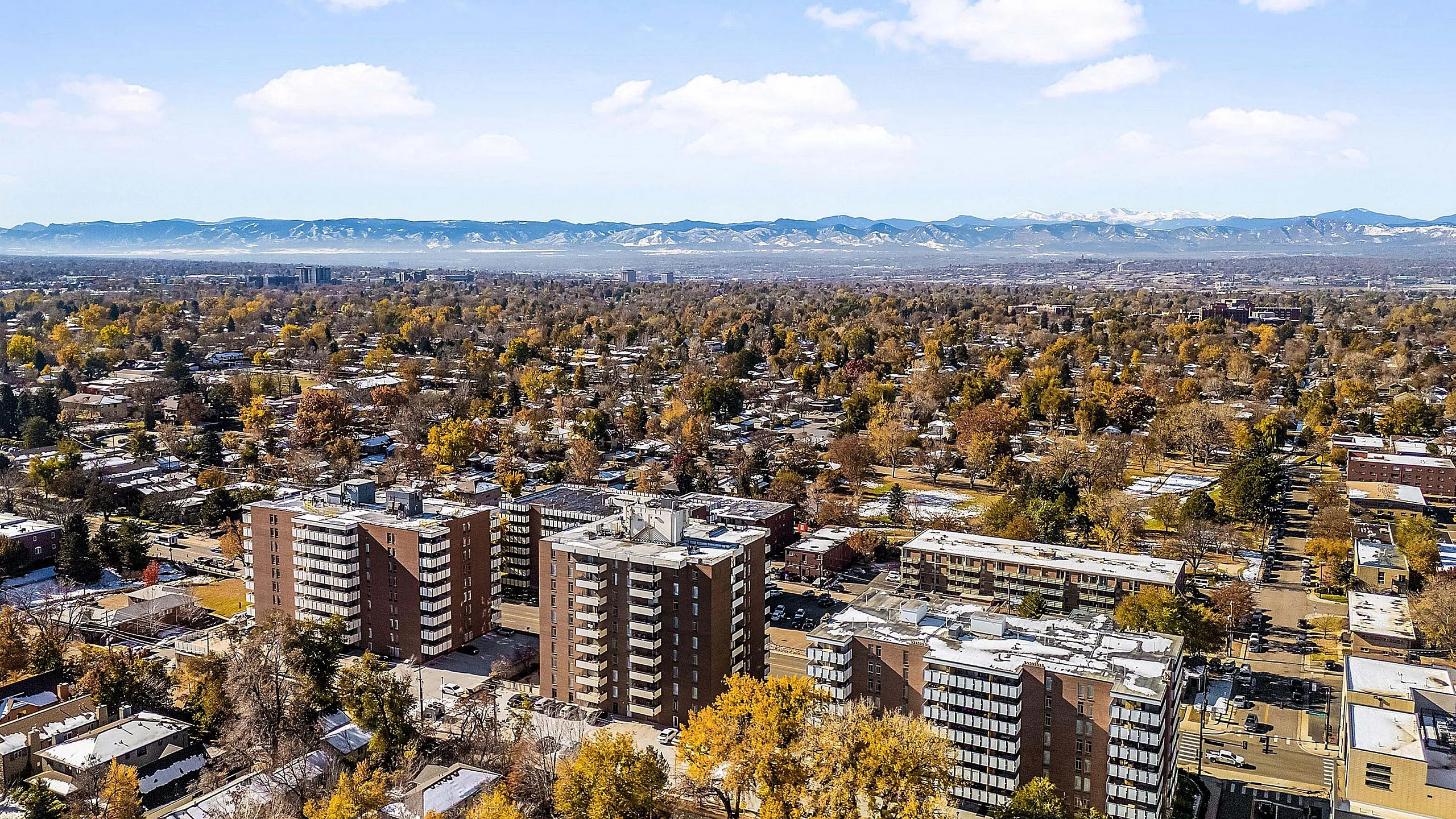 Breathtaking aerial view of a vibrant urban landscape with modern apartment buildings nestled among lush trees, offering panoramic mountain views under a clear blue sky.
