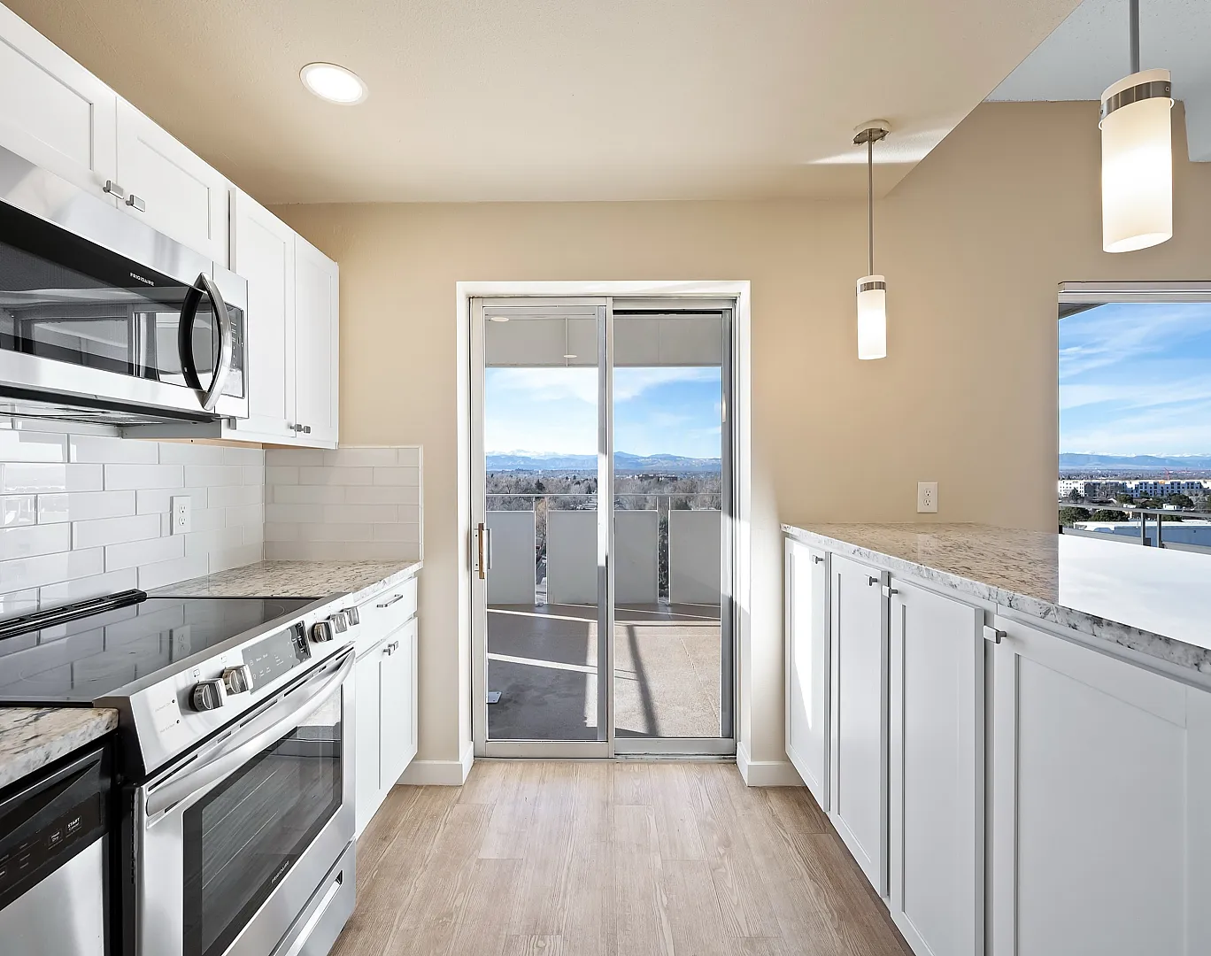 Modern kitchen with sleek white cabinets, stainless steel appliances, and a stunning mountain view through sliding glass doors.