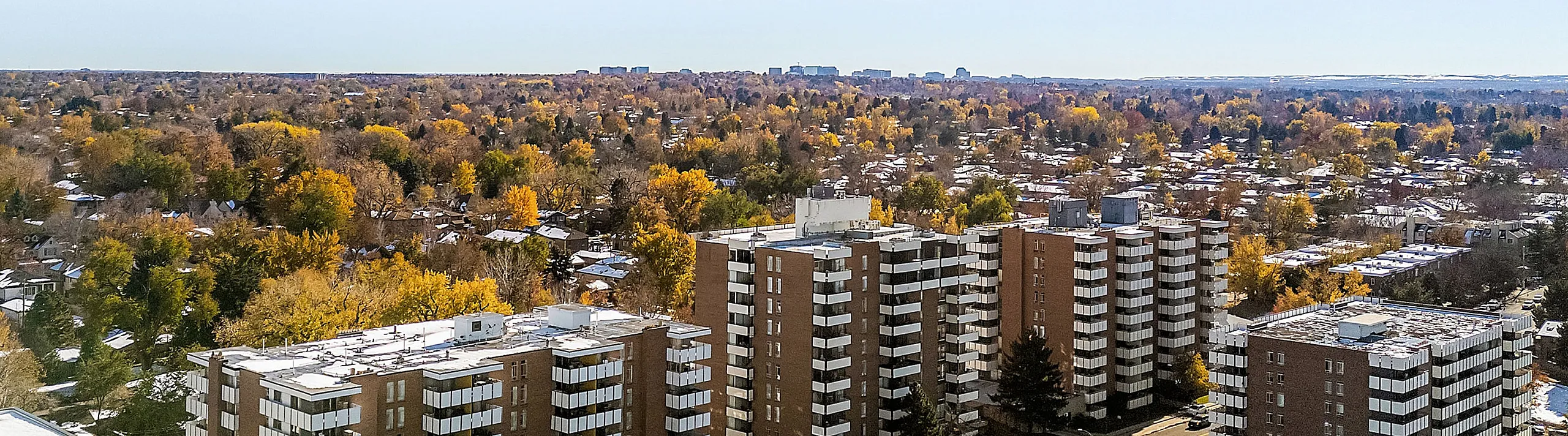 Scenic aerial view showcasing modern apartment buildings amidst a lush, autumnal landscape with vibrant foliage and expansive skies.